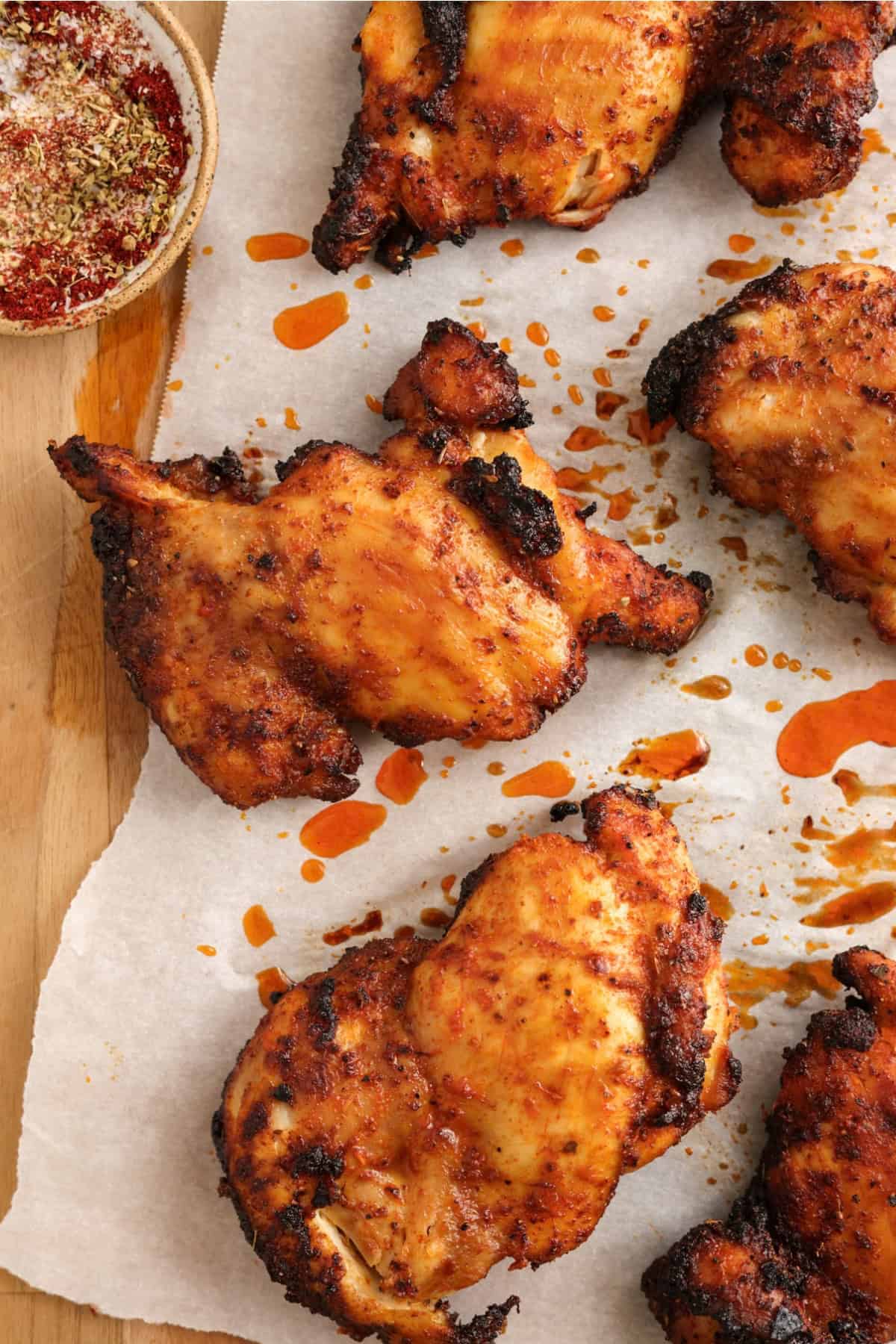 Air fryer chicken thighs on parchment paper, drizzled with cooking juices.