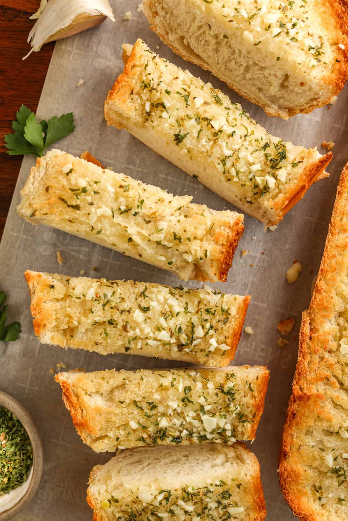 A loaf of sliced buttery garlic bread on parchment paper, garnished with fresh parsley.