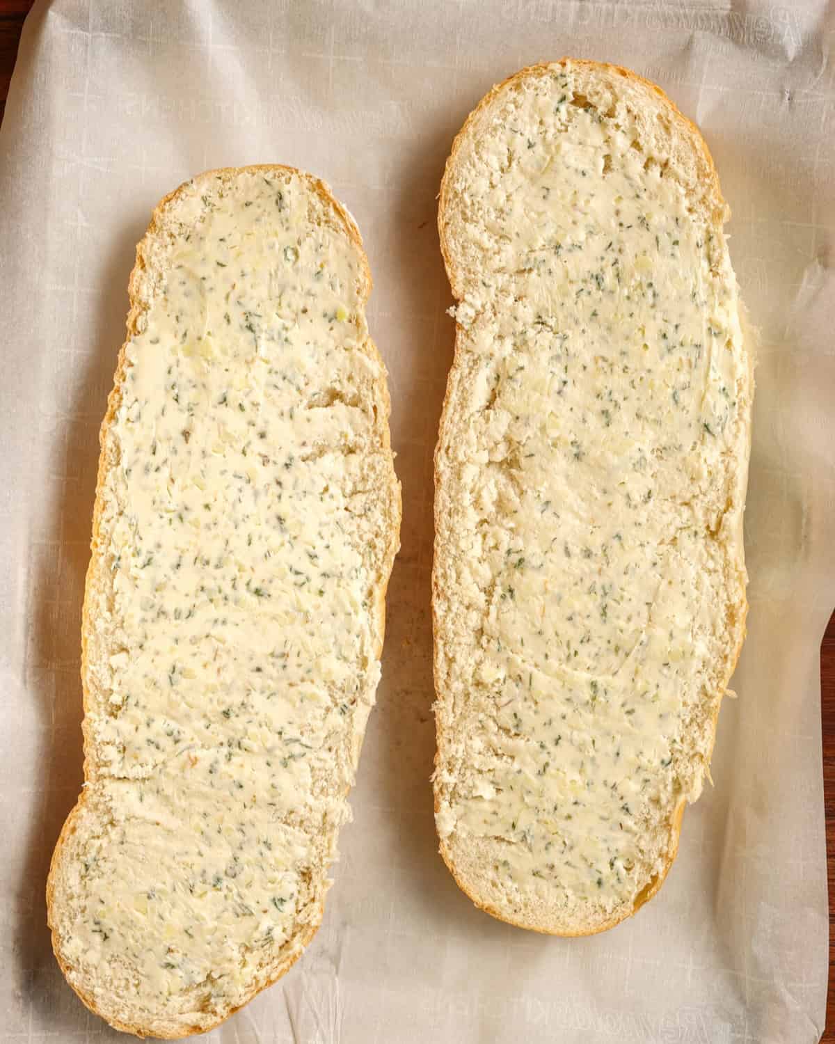 A loaf of Italian bread sliced open lengthwise, slathered in garlic butter.